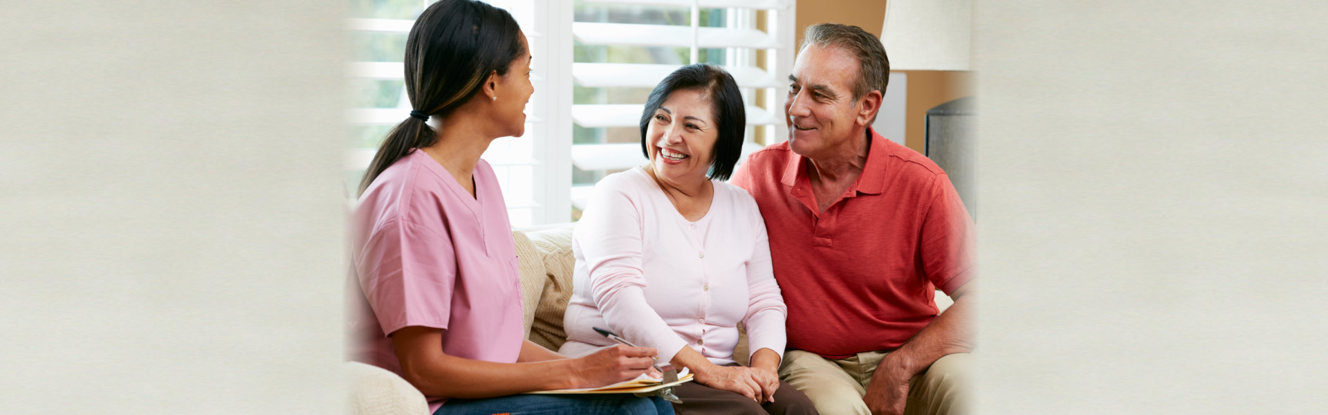 Nurse Making Notes During Home Visit With Senior Couple Smiling