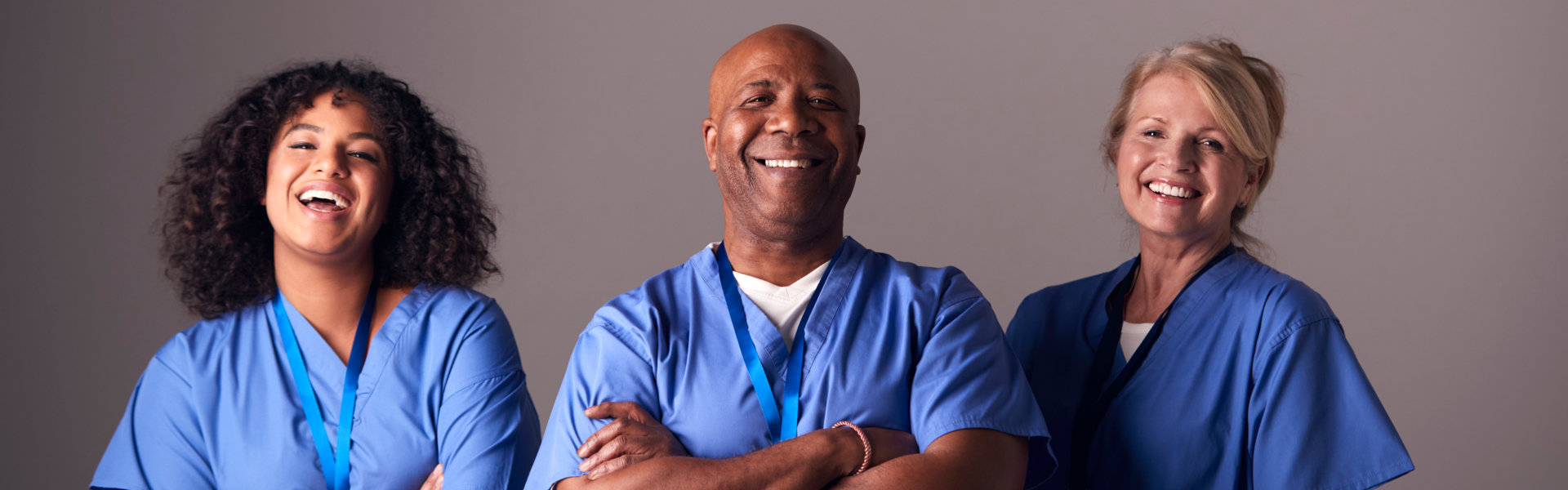 Members Of Surgical Team Wearing Scrubs Standing Against Grey Background