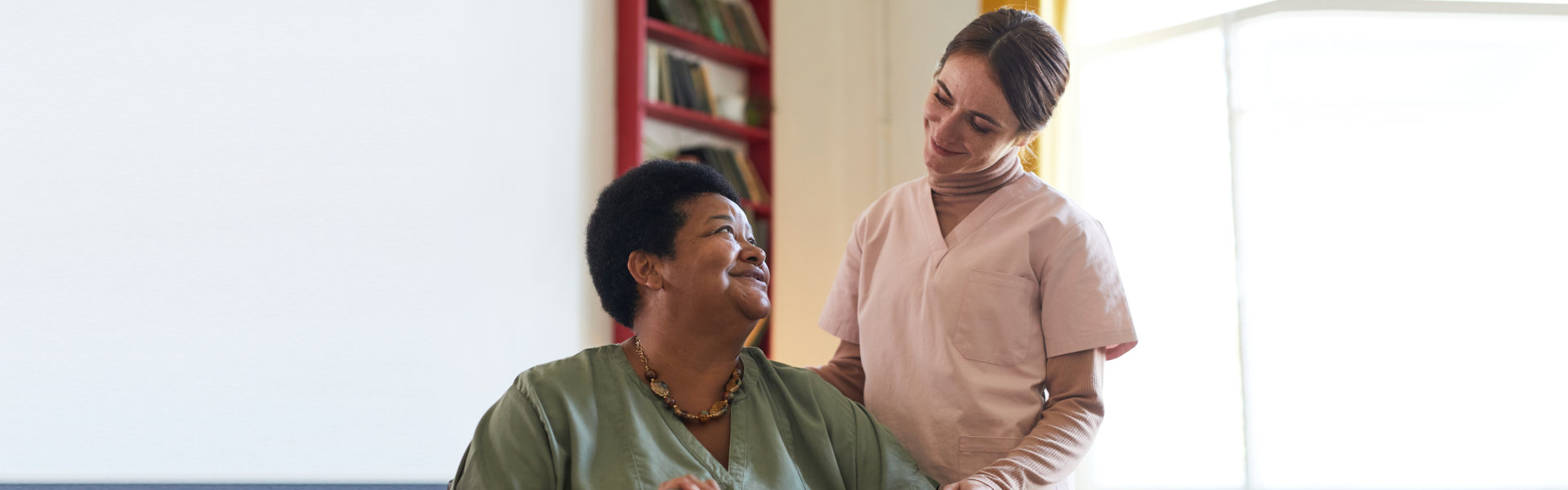 smiling young woman assisting female patient during dinner at nursing home
